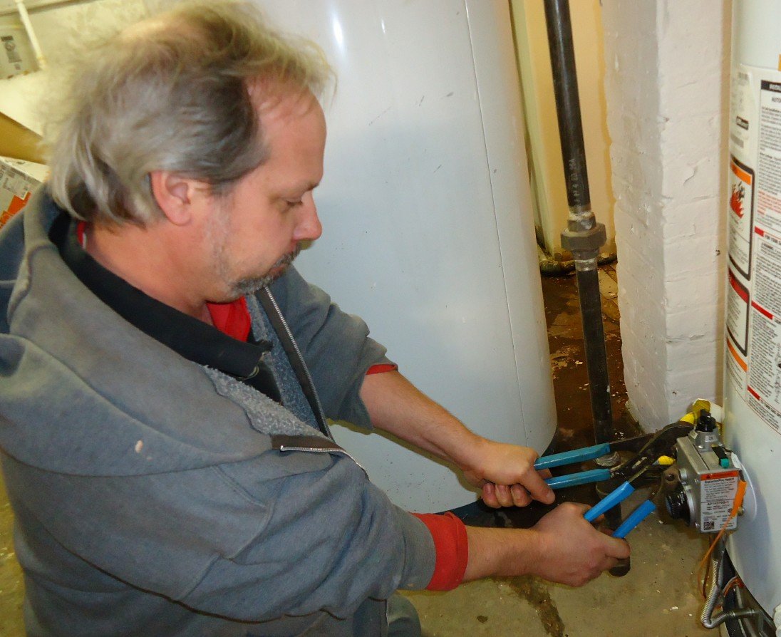 Plumber repairing a water heater fitting with two tools